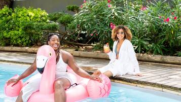 Two individuals in a swimming pool with one person seated on a pink inflatable float.