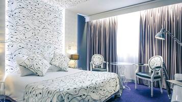 Ett hotellrum med en säng, två stolar, ett litet bord, en lampa och ett fönster med gardiner.