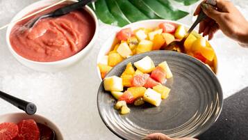 A person serving fruit onto a plate, with a bowl of pink sauce and grapefruit slices on ice nearby.