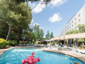 A swimming pool with lounge chairs and umbrellas, surrounded by trees and a hotel building.