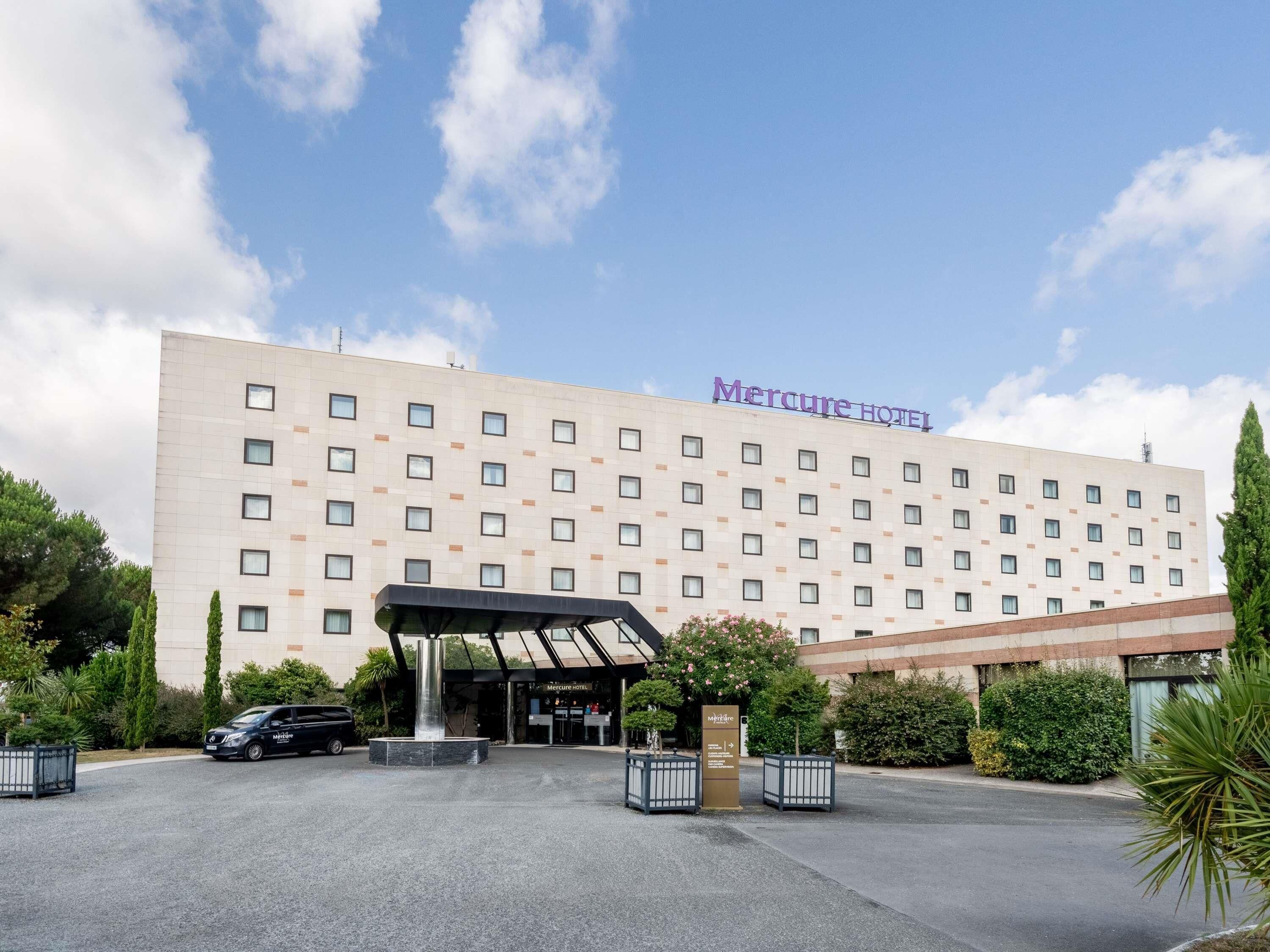 Un hotel con fachada moderna, un acceso cubierto y una zona de estacionamiento.