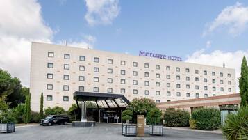 Un hotel con fachada moderna, un acceso cubierto y una zona de estacionamiento.