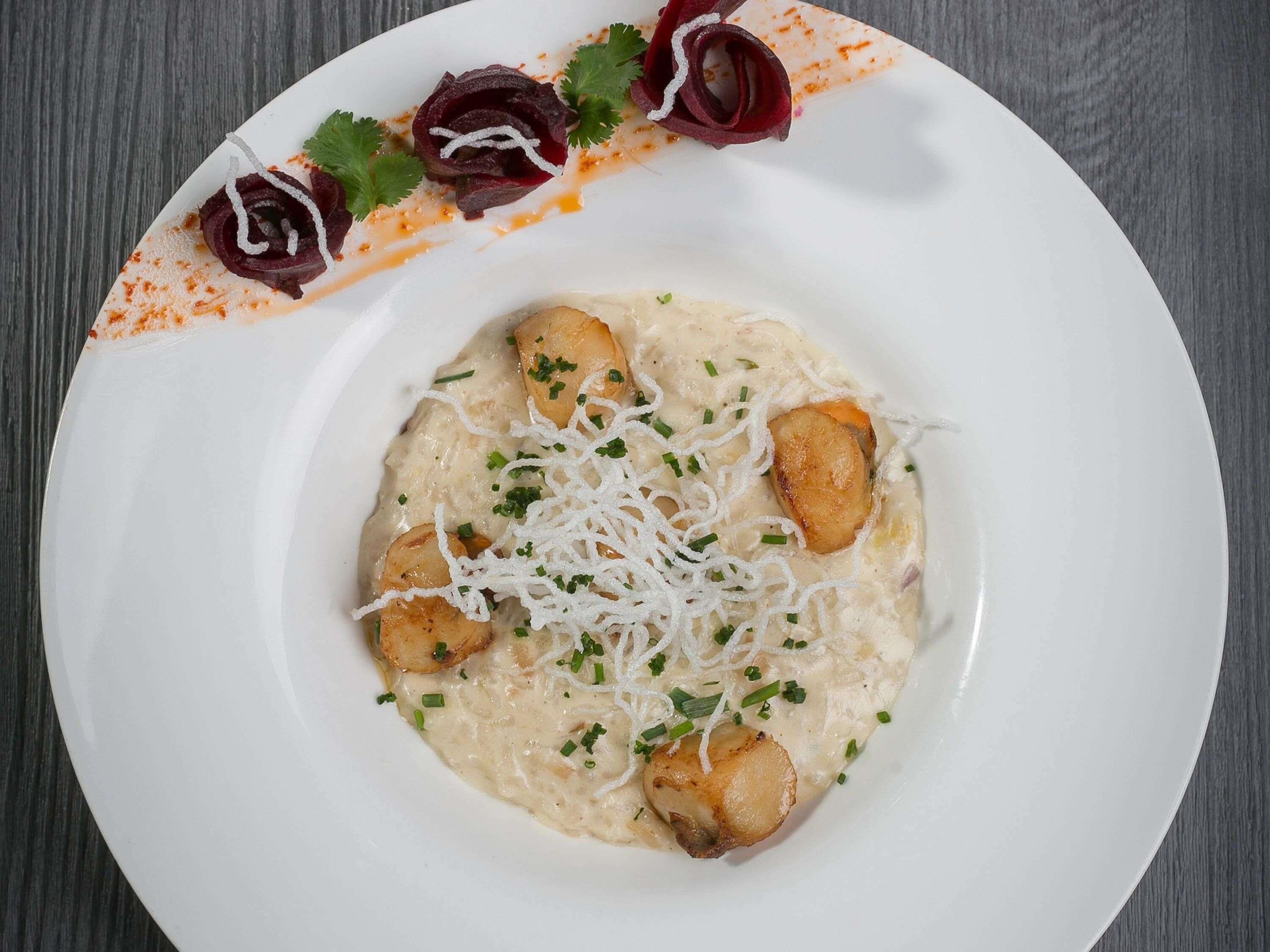 Um prato branco com um prato cremoso, guarnecido com ervas picadas e queijo ralado, acompanhado por fatias de beterraba e uma guarnição crocante.