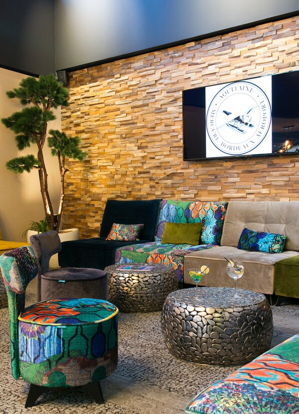 A modern lounge area with a stone wall, a mounted television, and colorful seating.