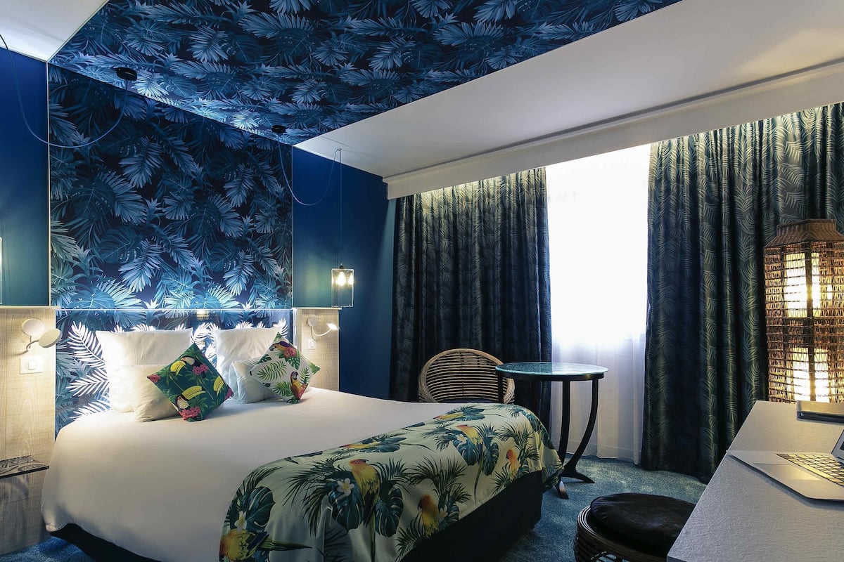 A hotel room with a bed, a desk, a chair, and a window with curtains.