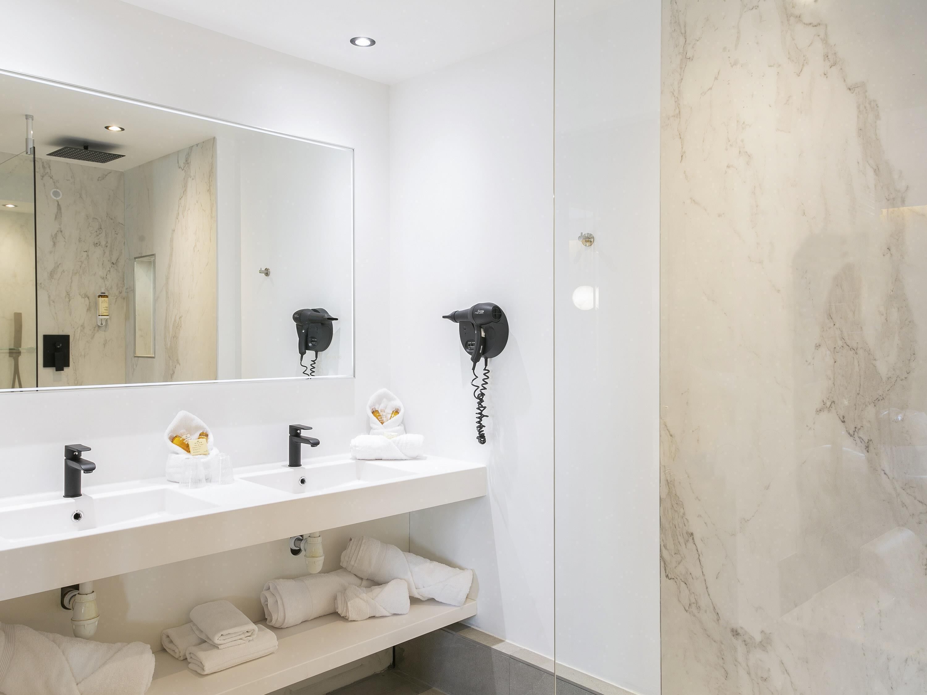 Ein modernes Badezimmer mit einem großen Spiegel, zwei Waschbecken, einem Fön und einem Handtuchhalter.