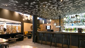 A bar area with a wooden counter, stools, and a variety of bottles.