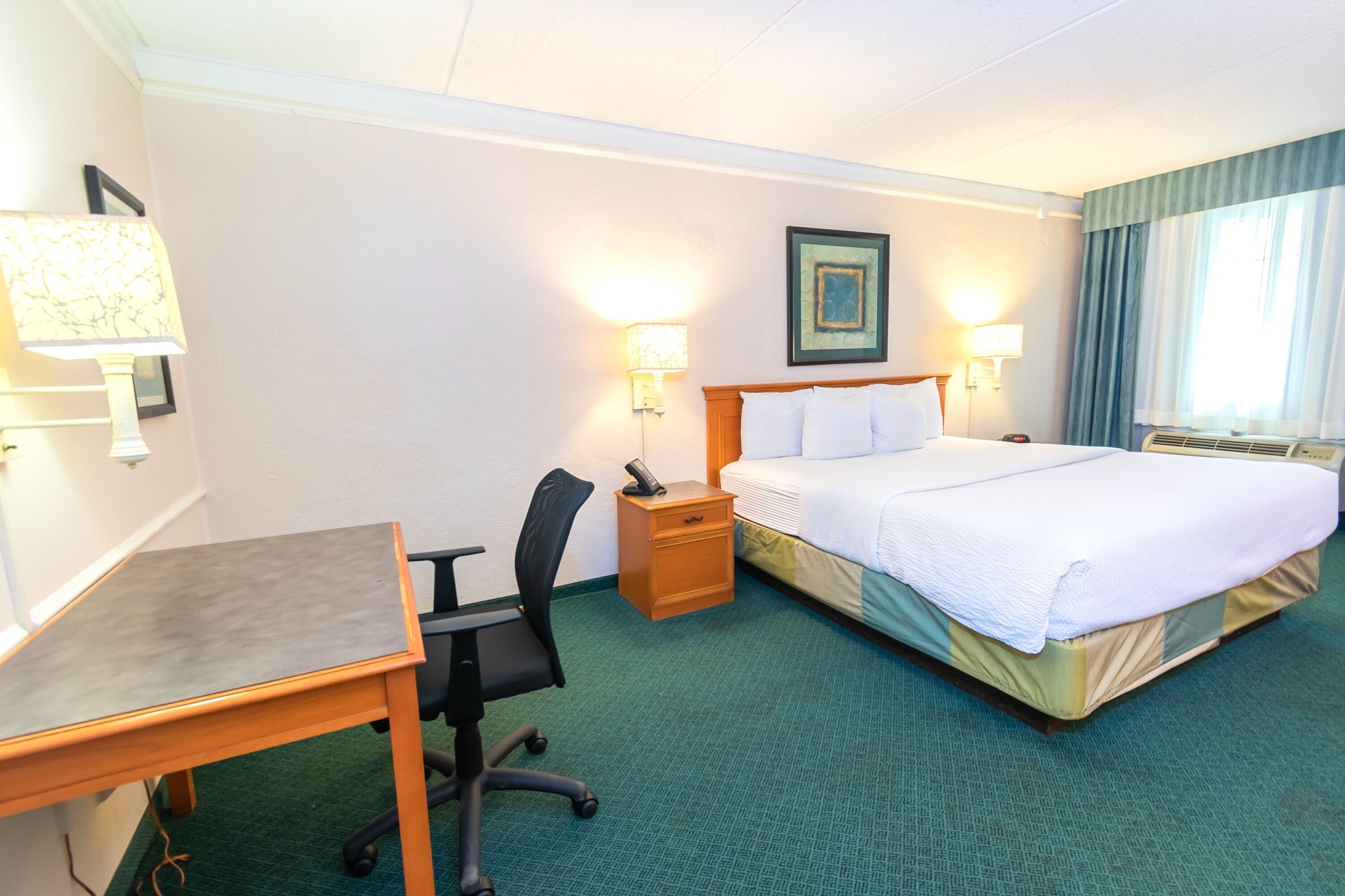Ein Hotelzimmer mit Bett, Schreibtisch, Stuhl, Nachttisch und zwei Wandleuchten.