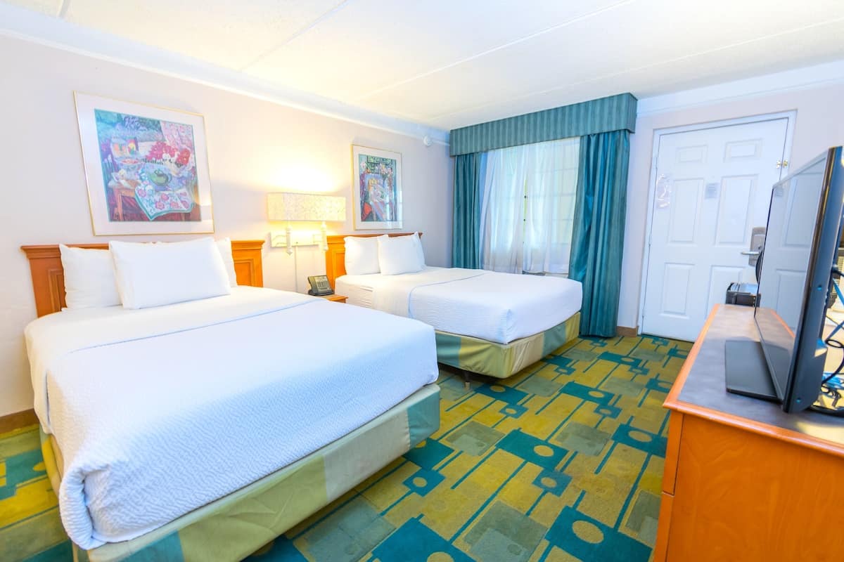 Habitación de hotel con dos camas, un escritorio con computadora y obras de arte en las paredes.