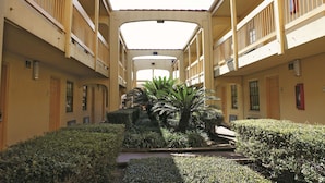A multi-story building with balconies, a central courtyard with plants, and a flat roof structure.