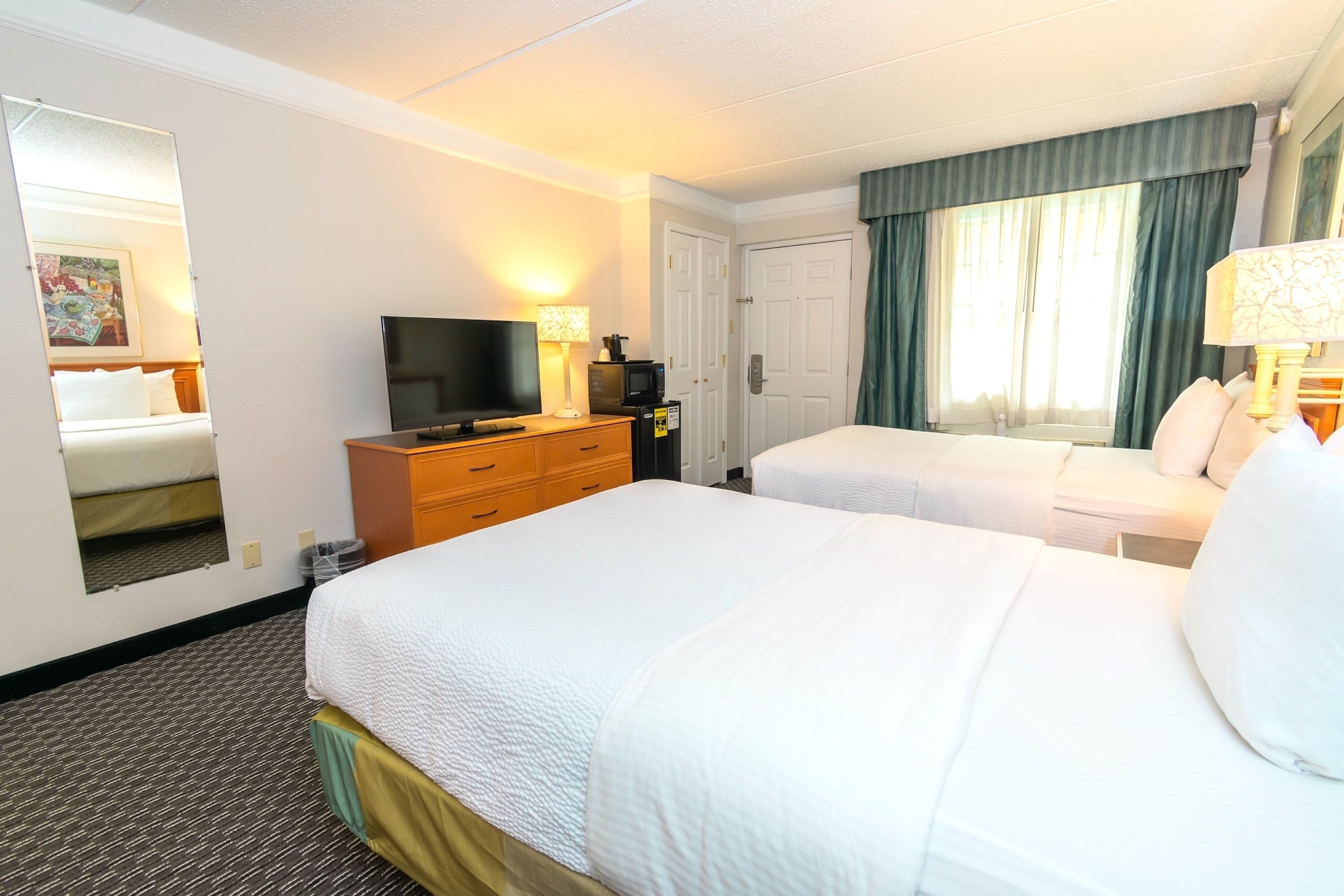 A hotel room with two beds, a television, a desk, and a mirror.