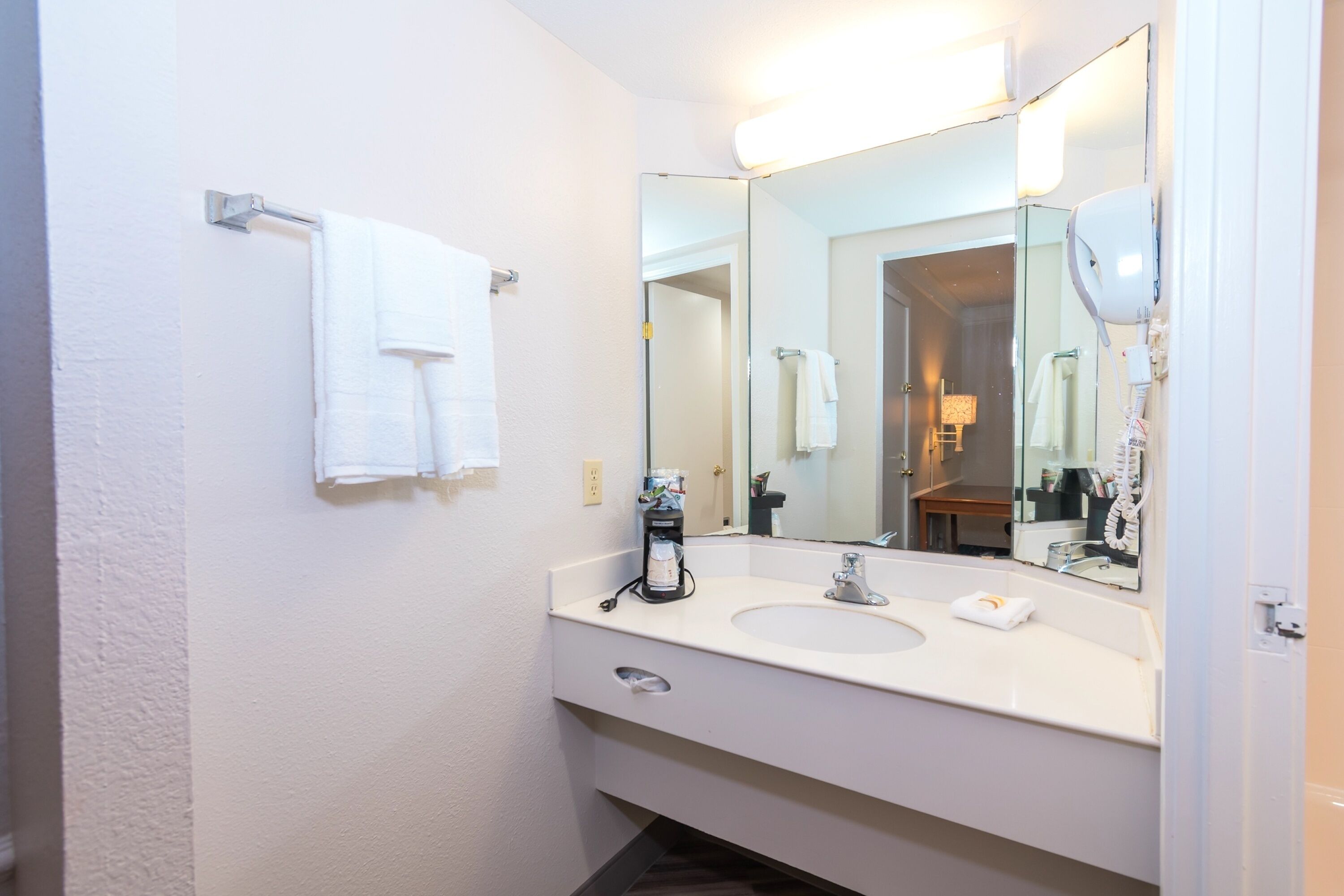 Un bagno con un lavandino bianco, uno specchio grande e un portascopevoli.