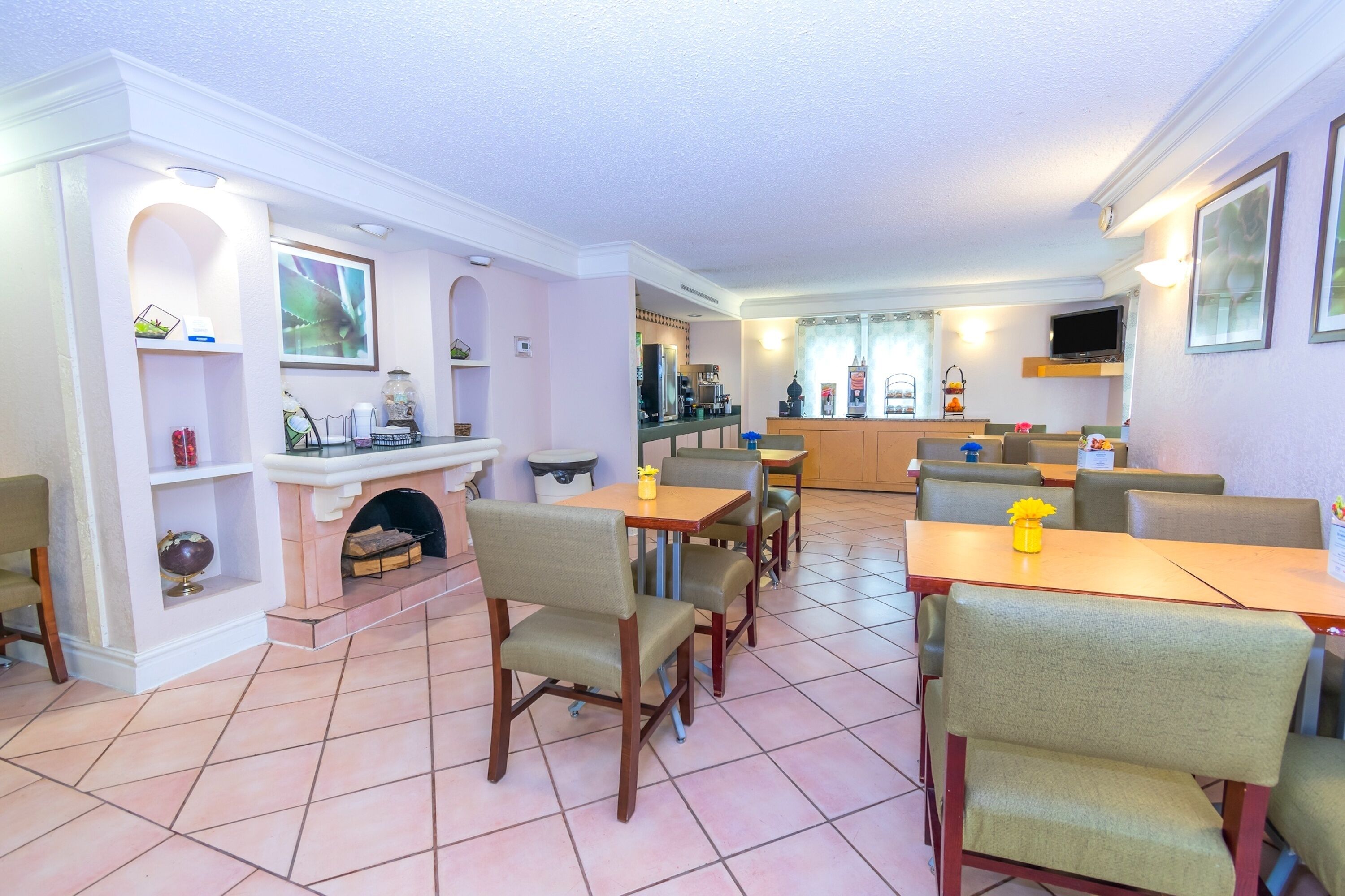 A dining area with multiple tables and chairs, a fireplace, and a kitchen in the background.