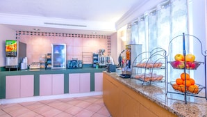A hotel reception area with a self-service beverage station, a coffee machine, and a fruit display.