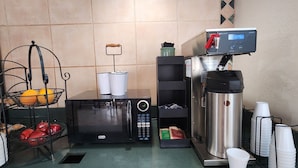 A kitchenette with a microwave, coffee machine, and a fruit basket.