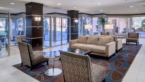 A lobby with a beige sofa, patterned armchairs, a coffee table, and a patterned rug. - Embassy Suites by Hilton St. Louis Airport (Bridgeton)
