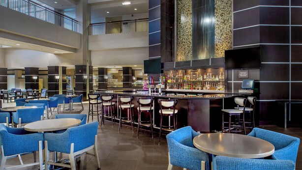 A modern hotel lobby with multiple seating areas, a bar, and a high ceiling with a balcony. - Embassy Suites by Hilton St. Louis Airport (Bridgeton)