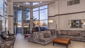 A spacious lobby with a large seating area, including sofas and armchairs, and a large window offering a view of the outside. - Embassy Suites by Hilton St. Louis Airport (Bridgeton)