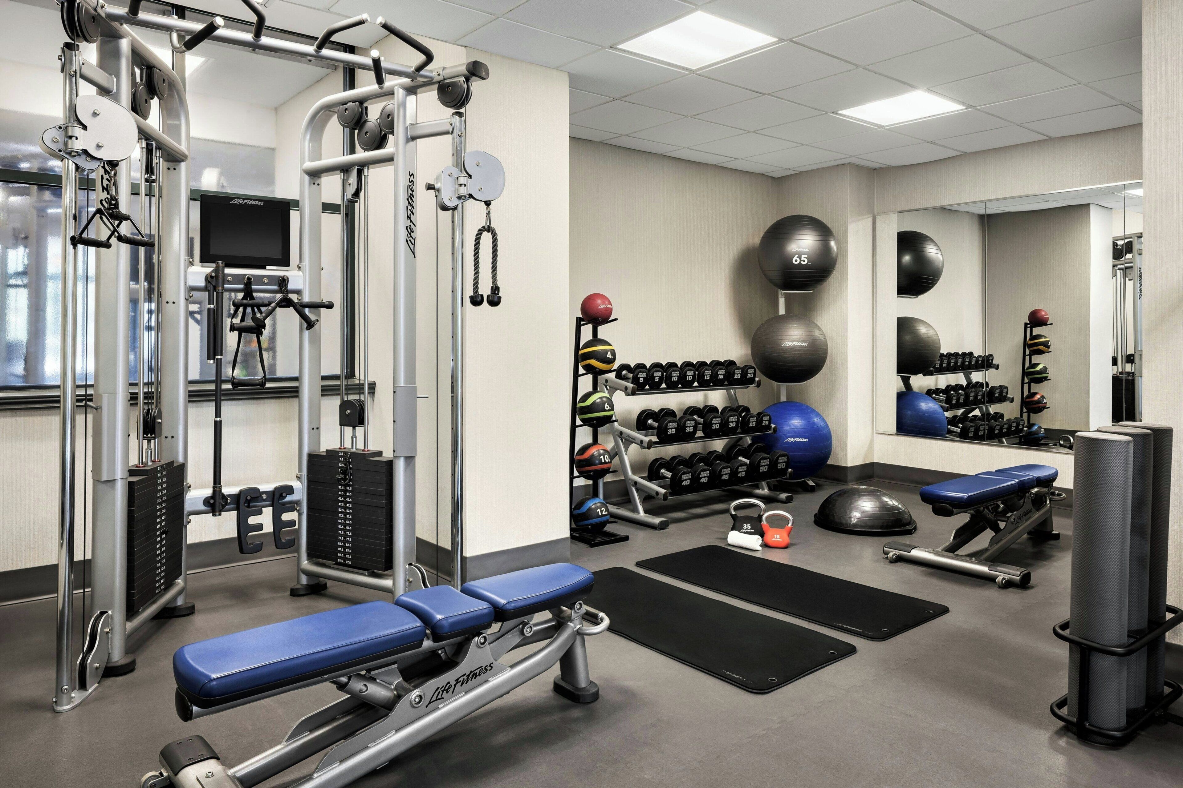 A gym with weight machines, dumbbells, medicine balls, and a bench.