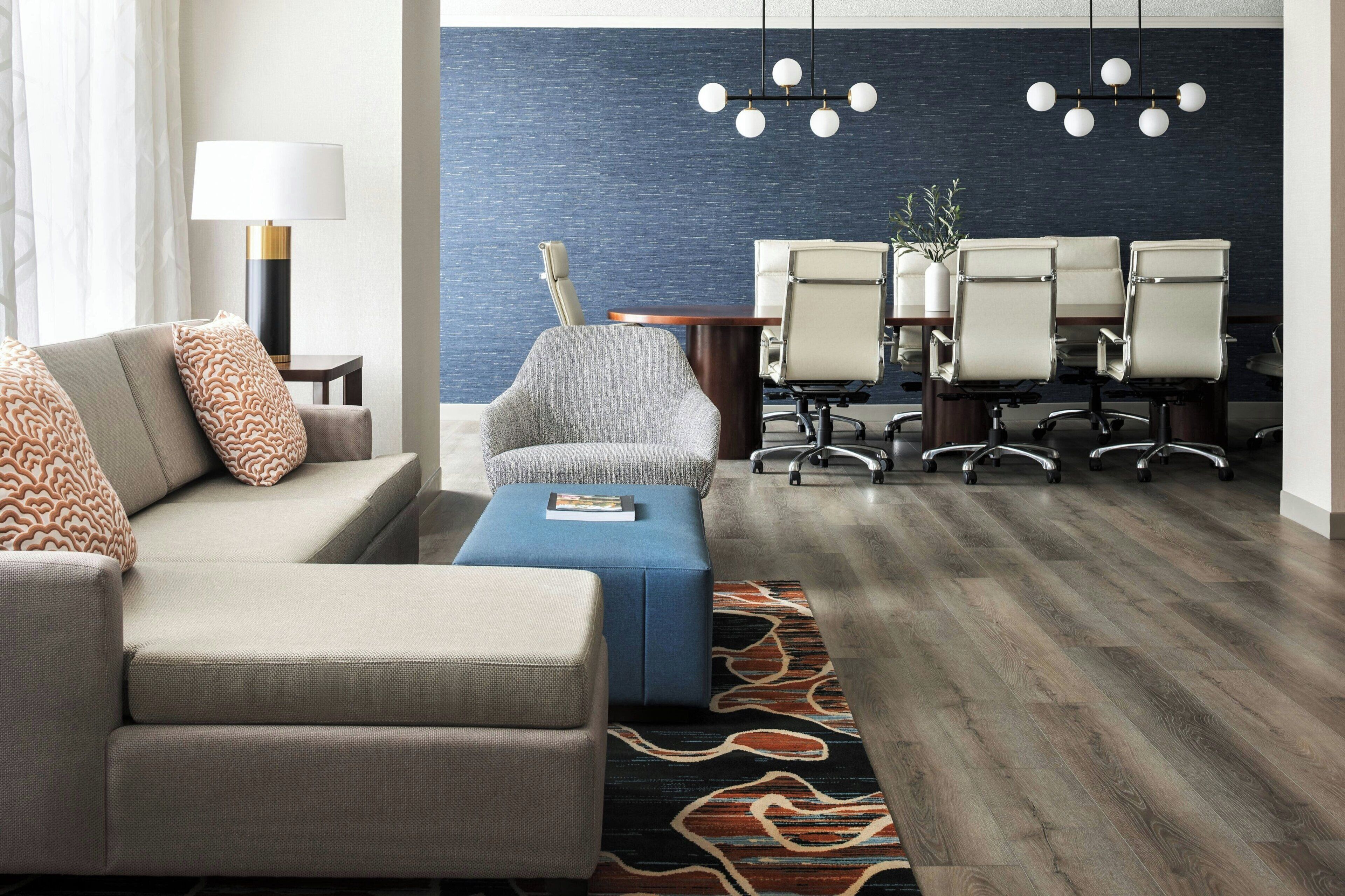 Una habitación de hotel moderna con sofá, reposapiés y una mesa de conferencias con sillas.