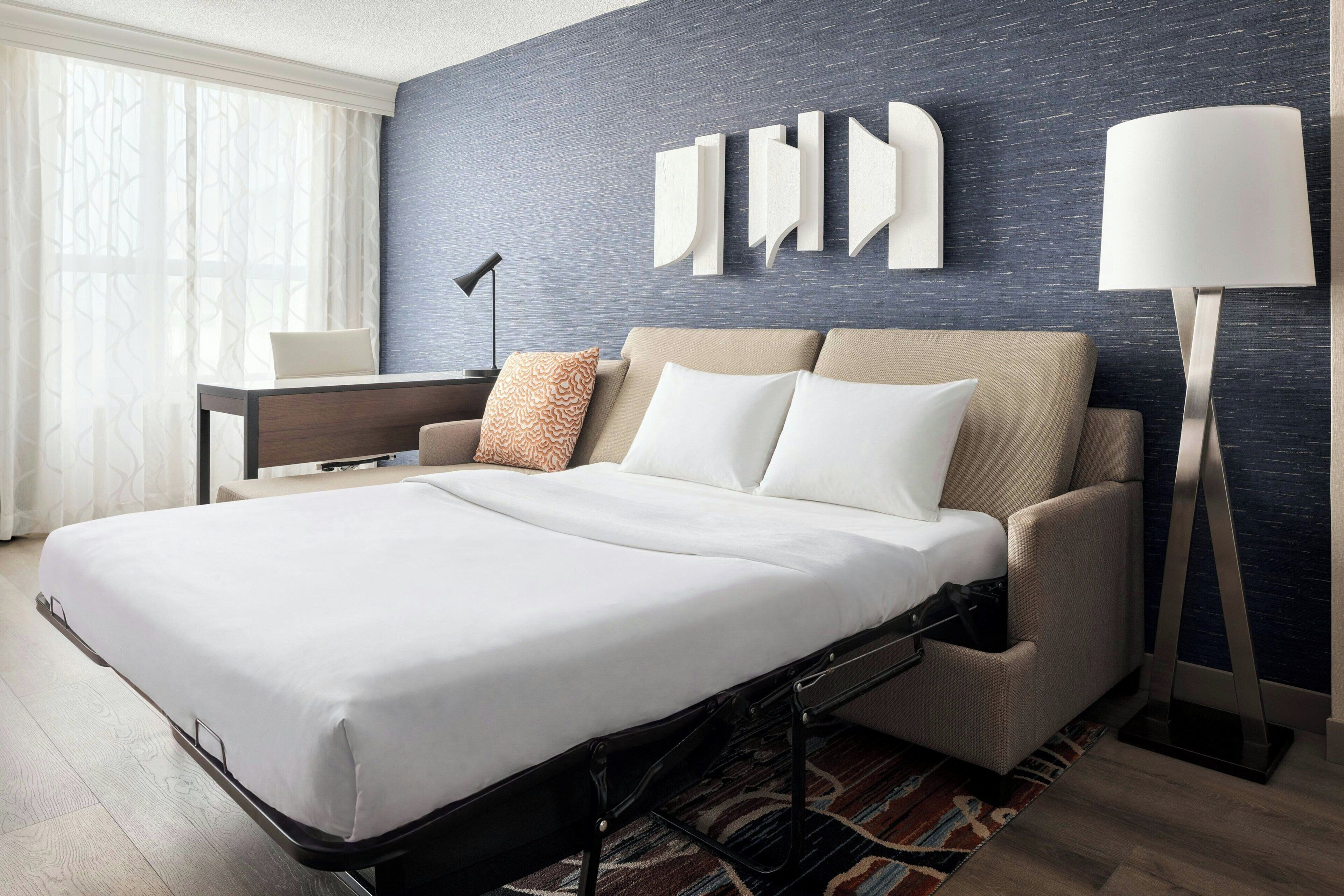 Habitación de hotel con cama, escritorio, lámpara y una pared decorada con arte abstracto.