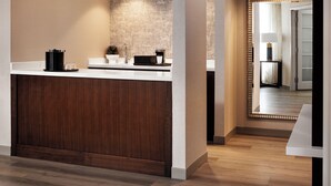 A modern hotel lobby with a wooden reception desk, a patterned wall, and a mirror reflecting the room. - Chicago Marriott Suites Deerfield (Deerfield)
