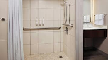 A shower with a handrail, a tiled floor, and a small drain.