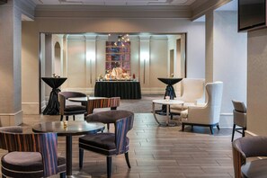 A hotel lobby with a reception desk, seating area, and a view of the bar.