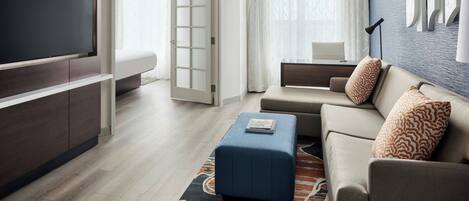 A modern hotel room with a flat-screen TV, a sofa, a coffee table, and a patterned rug.