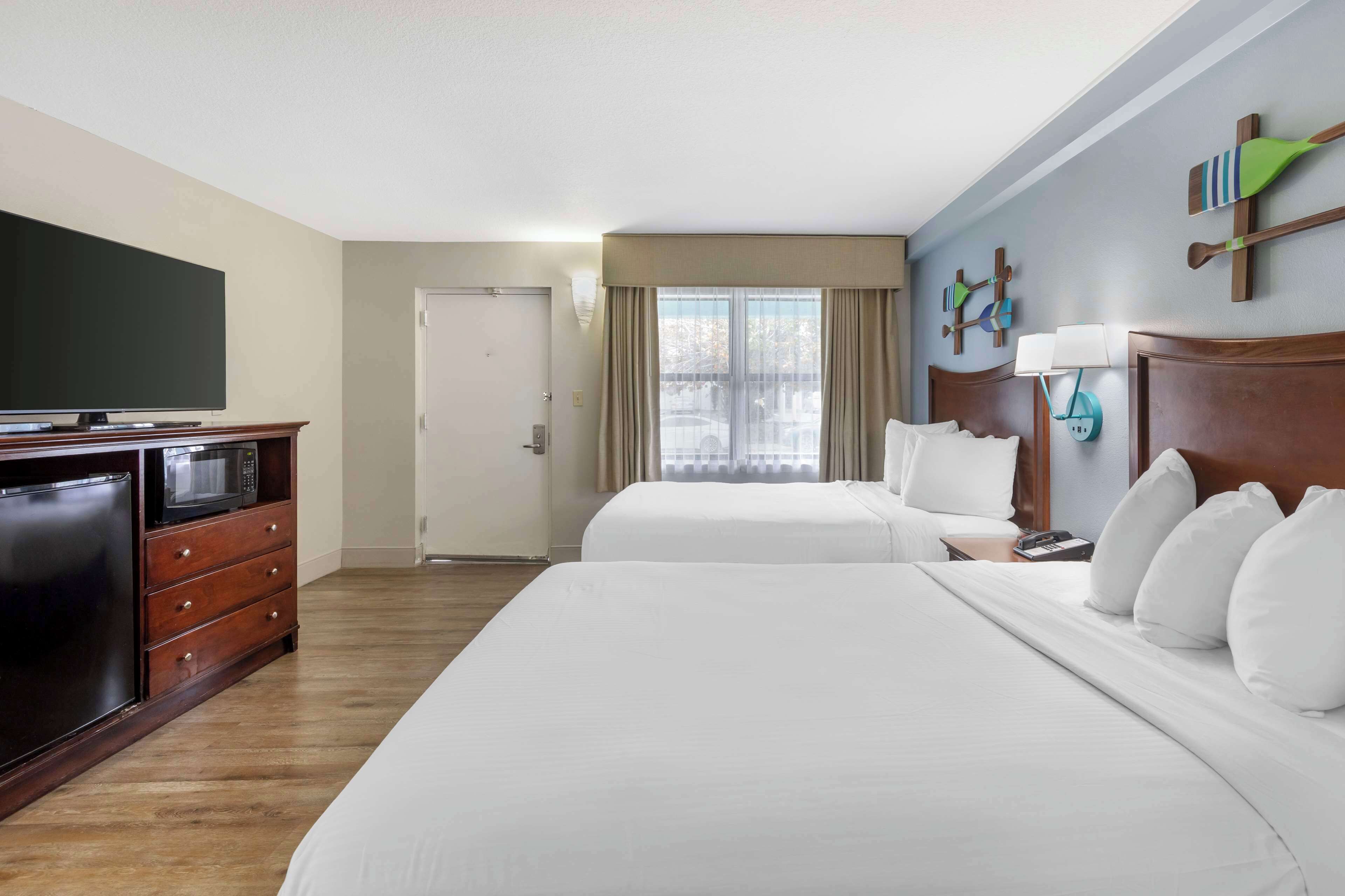 A hotel room with two beds, a TV, a microwave, a dresser, and a window with curtains.
