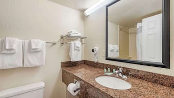 Ein Badezimmer mit einer weißen Toilette, einem Waschbecken mit Granitplatte, einem Handtuchhalter mit gefalteten Handtüchern, einem Händetrockner und einem großen Spiegel.