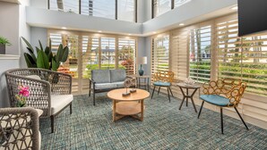 A spacious indoor area with wicker furniture, a round coffee table, and large windows offering views of greenery outside. - Best Western Cocoa Beach - Port Canaveral (Cocoa Beach)