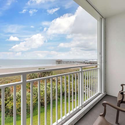 A balcony with a view of the beach and pier, featuring two wicker chairs.