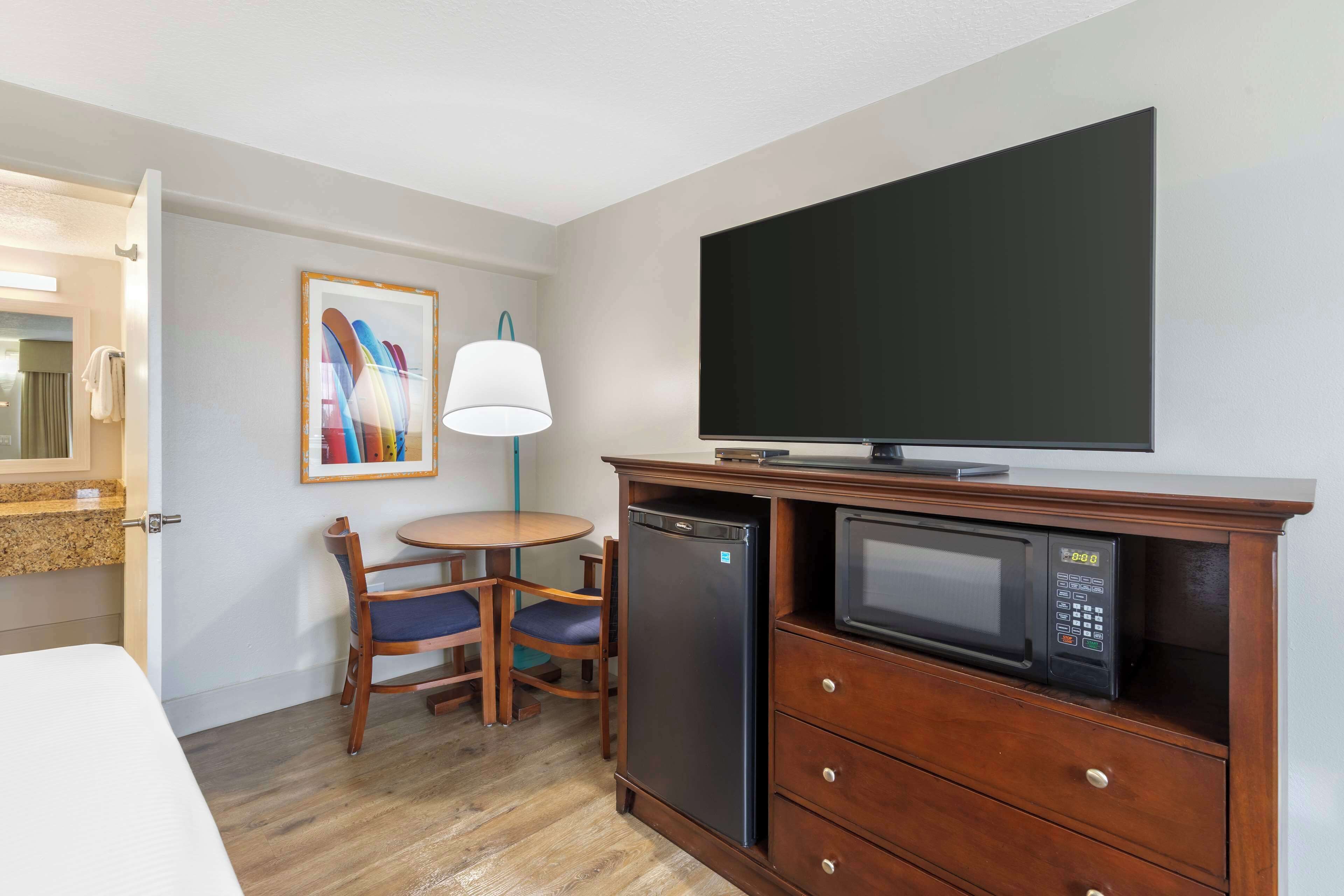 Une chambre d’hôtel de taille réduite comprenant un lit, une petite table à manger avec des chaises, un four à micro-ondes, un réfrigérateur, une télévision et un tableau accroché au mur.