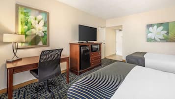 A hotel room with a bed, a desk, a chair, a television on a cabinet, and two paintings on the walls.