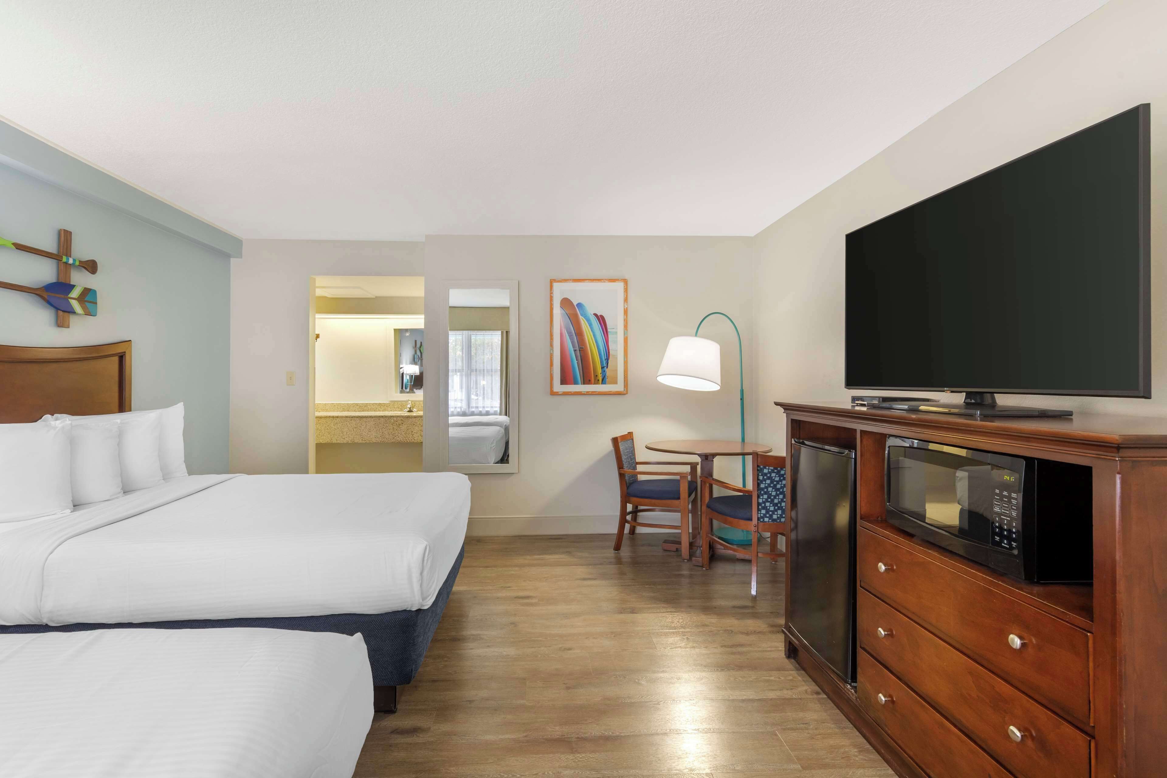 A hotel room with two beds, a TV, a microwave, a dining table with chairs, and a mirror.