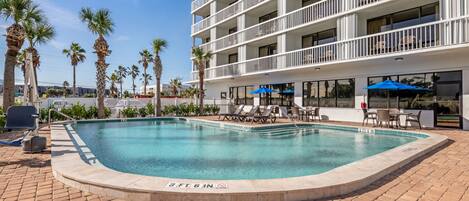 A hotel pool area with a clear blue pool, lounge chairs, and umbrellas.