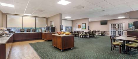 A spacious kitchen area with a buffet setup, a dining area with tables and chairs, and a view of the outdoors through large windows.