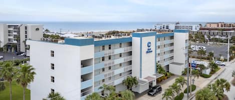 A multi-story hotel with a blue and white exterior, a visible pool, and a view of the beach.