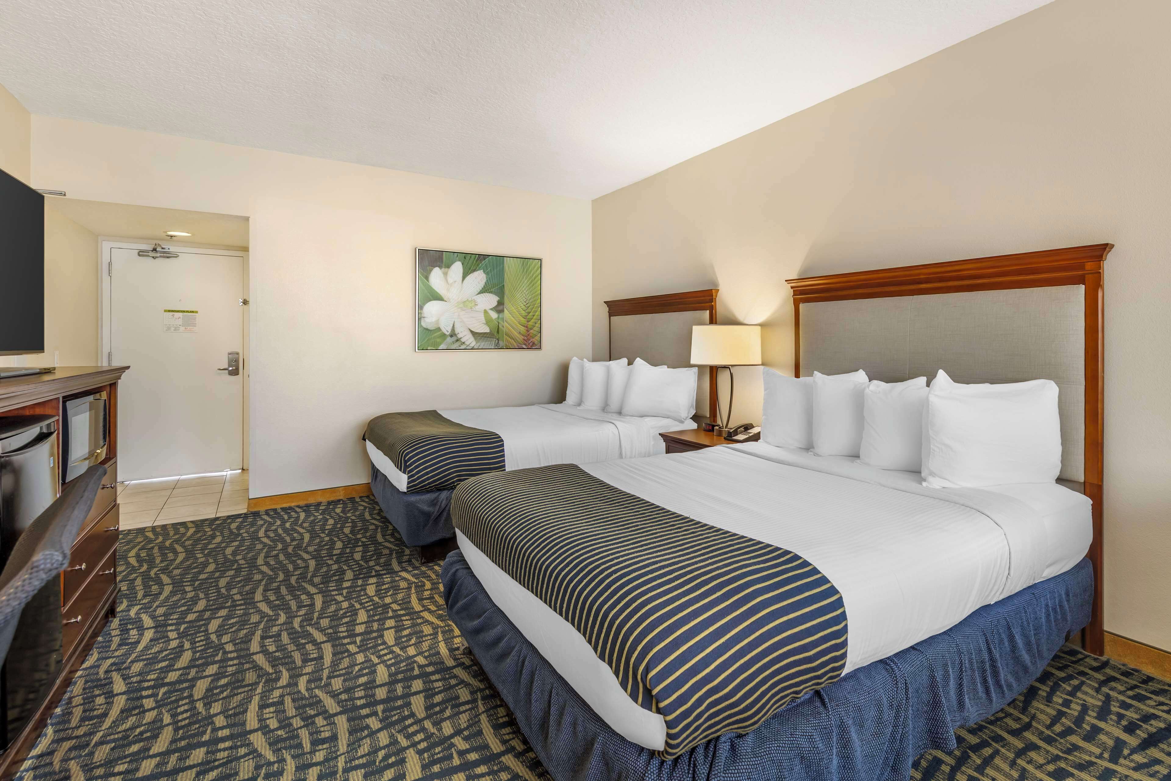 A hotel room with two beds, a desk with a chair, a lamp, and a painting on the wall.