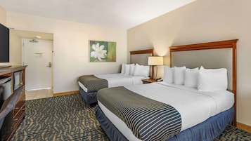A hotel room with two beds, a desk with a chair, a lamp, and a painting on the wall.