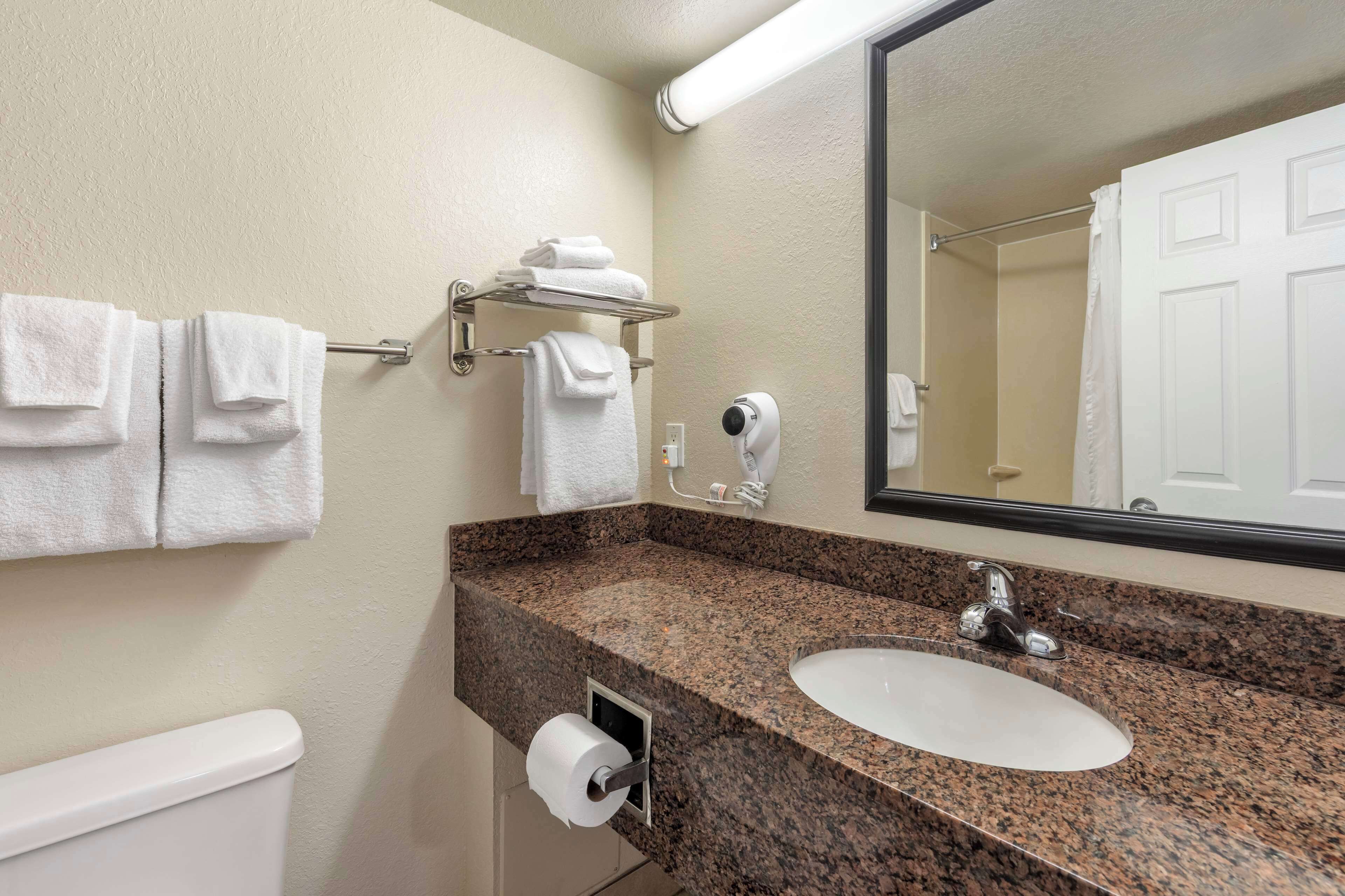 A bathroom with a granite countertop, white sink, and a towel rack with folded towels.