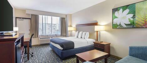 A hotel room with a bed, desk, chair, and a large window with curtains.