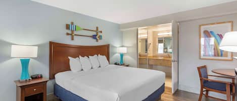 A hotel room with a large bed, two bedside tables with lamps, a wooden headboard, a small table with a chair, and a mirror.