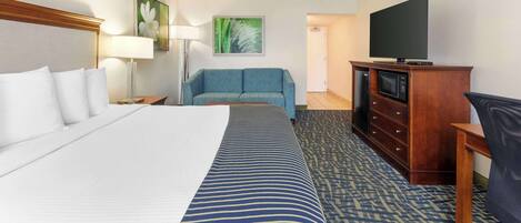 Ein Hotelzimmer mit einem großen Bett, einer Couch, einem Fernseher auf einer Holzkommode und einem Schreibtisch.