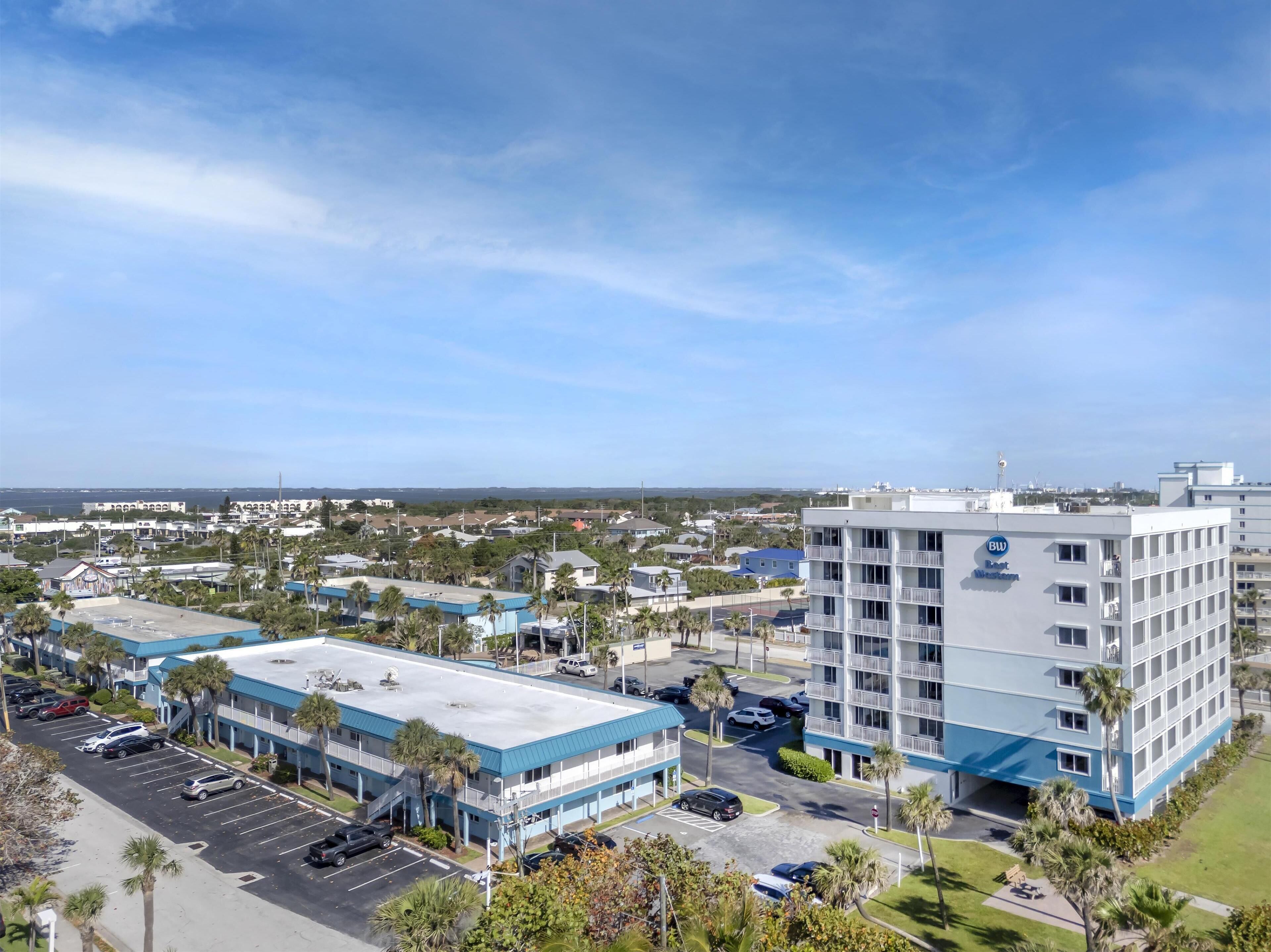 A hotel with a blue and white exterior, multiple floors, and a parking lot with cars.