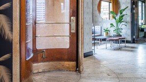 A hotel lobby with a wooden door, a round mirror, a seating area with a table and chairs, and a large potted plant. - Hotel Astoria, BW Signature Collection (Copenhagen)