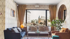 A modern living room with a sofa, armchair, coffee table, and a large window offering a city view. - Hotel Astoria, BW Signature Collection (Copenhagen)