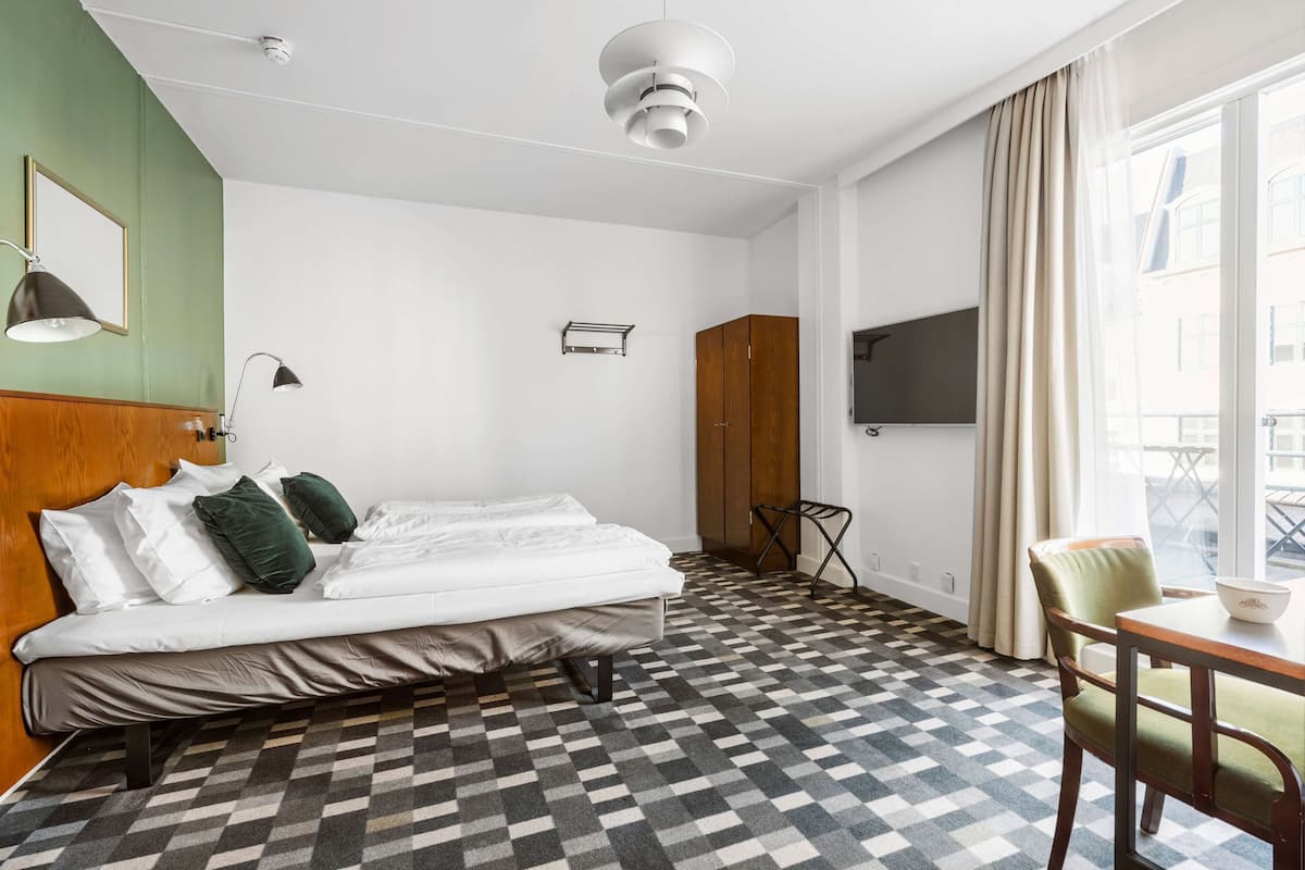 A hotel room with a bed, a desk, a chair, a TV, and a window with curtains.