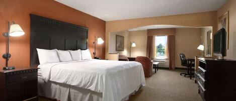 A hotel room with a large bed, bedside tables, a desk, a chair, a dresser, and a television.